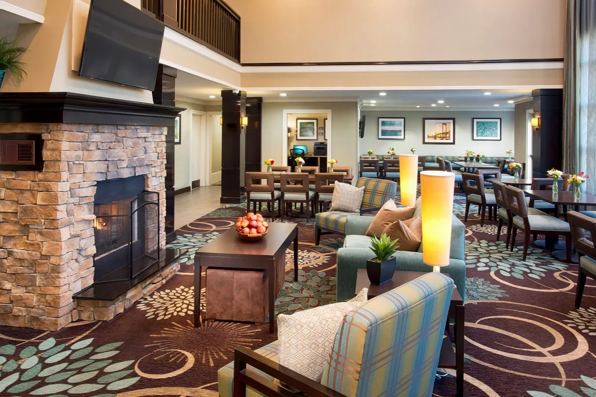 A spacious living area featuring a comfortable seating arrangement around a cozy fireplace, with the dining area visible in the background. Decorative plants add a homely touch. The scene radiates warmth and invites guests to relax, socialize, or settle in for a quiet evening.