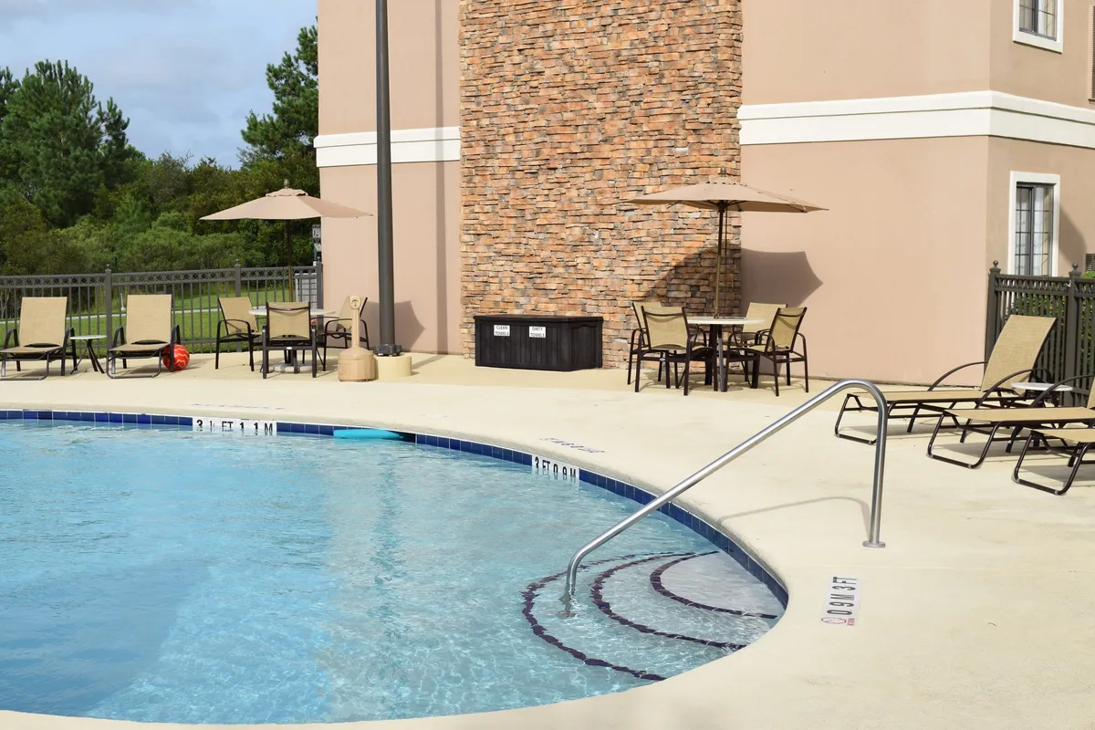 A vibrant outdoor swimming pool area with inviting lounge chairs, a striking stone feature wall, and colorful umbrellas. The mood is lively and family-friendly, with plenty of space for sunbathing, swimming, and relaxing together. The space is bathed in warm light, suggesting enjoyment during sunny days or early evenings.