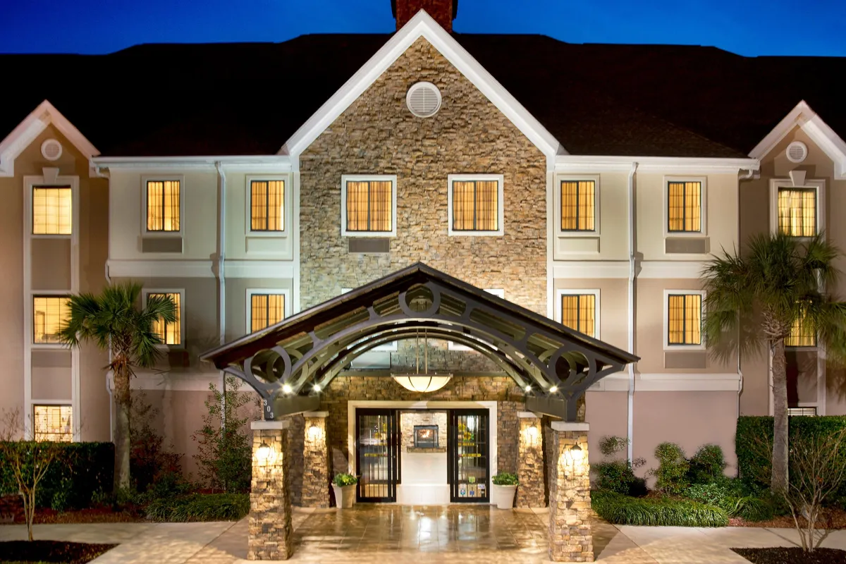 This image highlights the hotel's arched entrance framed by a stone facade and warmly illuminated windows. The scene evokes a sense of welcome and arrival, capturing guests as they check in or gather outside the main entrance. The lighting suggests early evening, hinting at both business and leisure activities that continue into the evening hours.