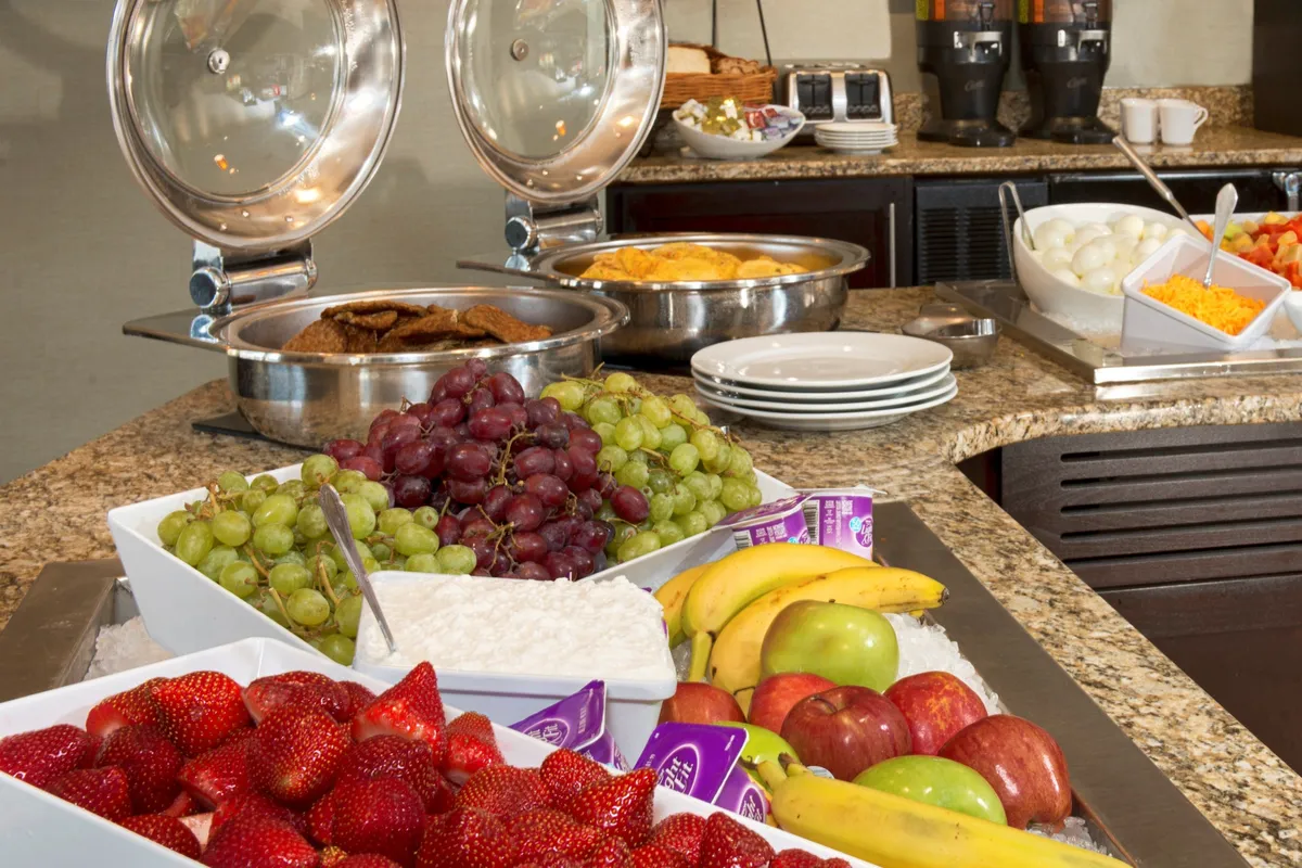 A close-up of fresh fruits, assorted breakfast items, and a cheerful coffee station, set in a bright indoor space. The scene conveys a sense of abundance and choice, reinforcing the idea of starting the day with a hearty breakfast or grabbing a quick bite in a comfortable, communal setting.